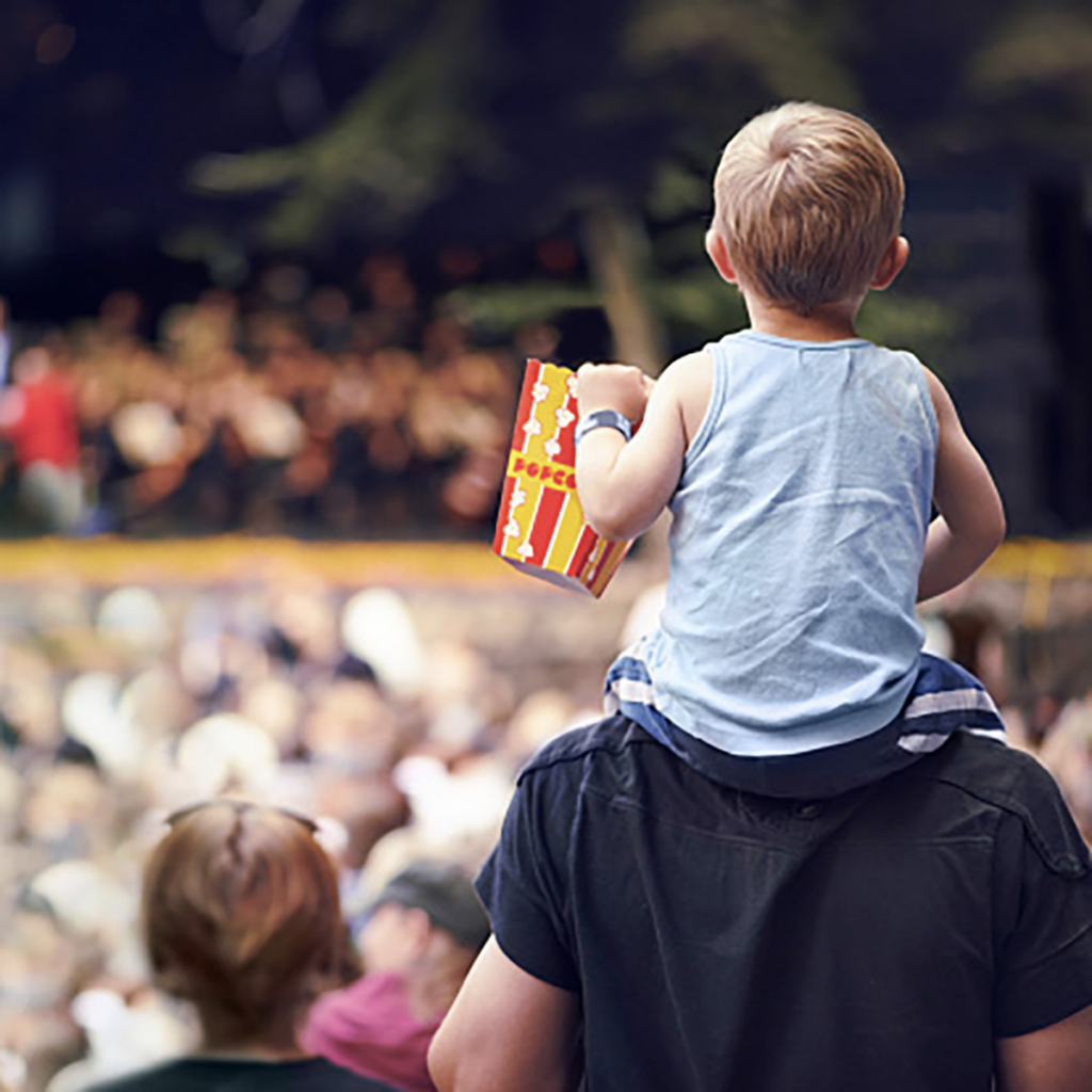 boy on his dad's shoulders eating popcorn at an outside event
